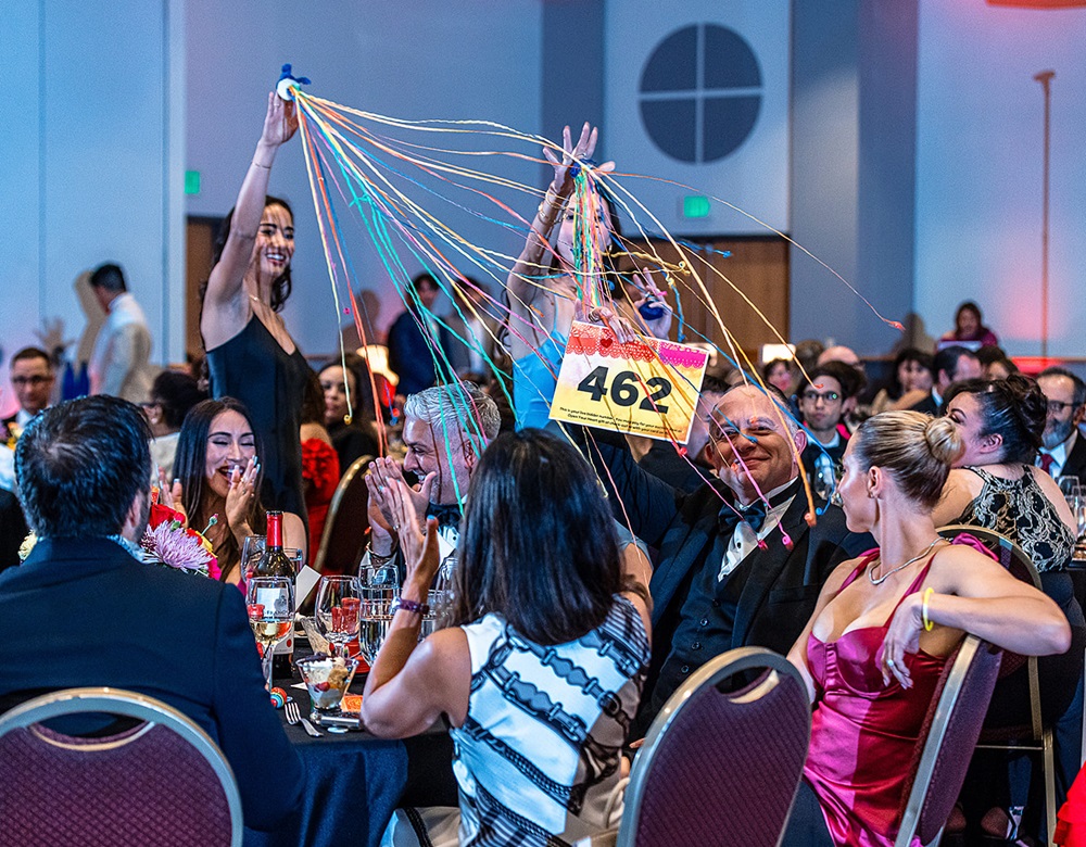 Two women setting off streamer bombs while a smiling man holds up bidder number 462.