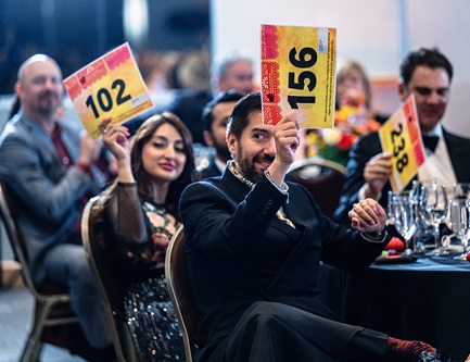 Three people seated at a table holding up bidder numbers 102, 156, and 238.