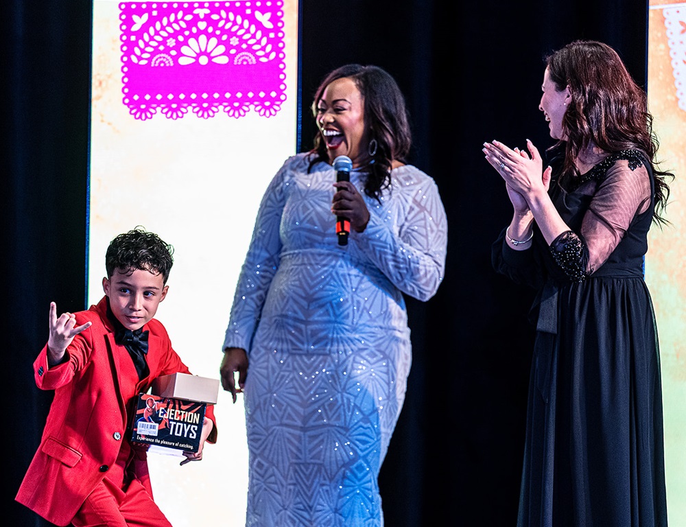 Two women and a young boy laughing and clapping on stage.